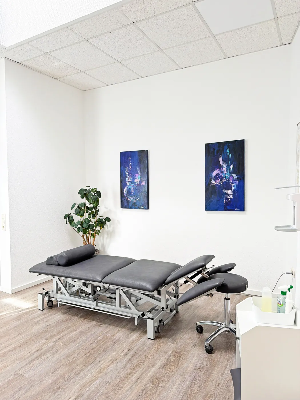Heller Behandlungsraum mit höhenverstellbarer Therapieliege und Rollhocker