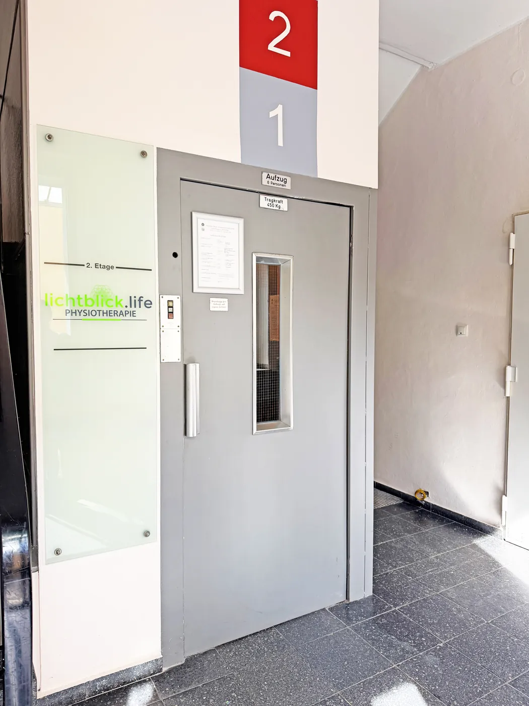 Hauseingang mit Aufzug und Praxisschild lichtblick.life Physiotherapie in der 2. Etage